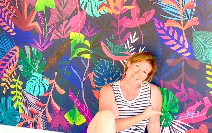 woman in striped shirt and blue shorts sitting by colorful living room wall mural