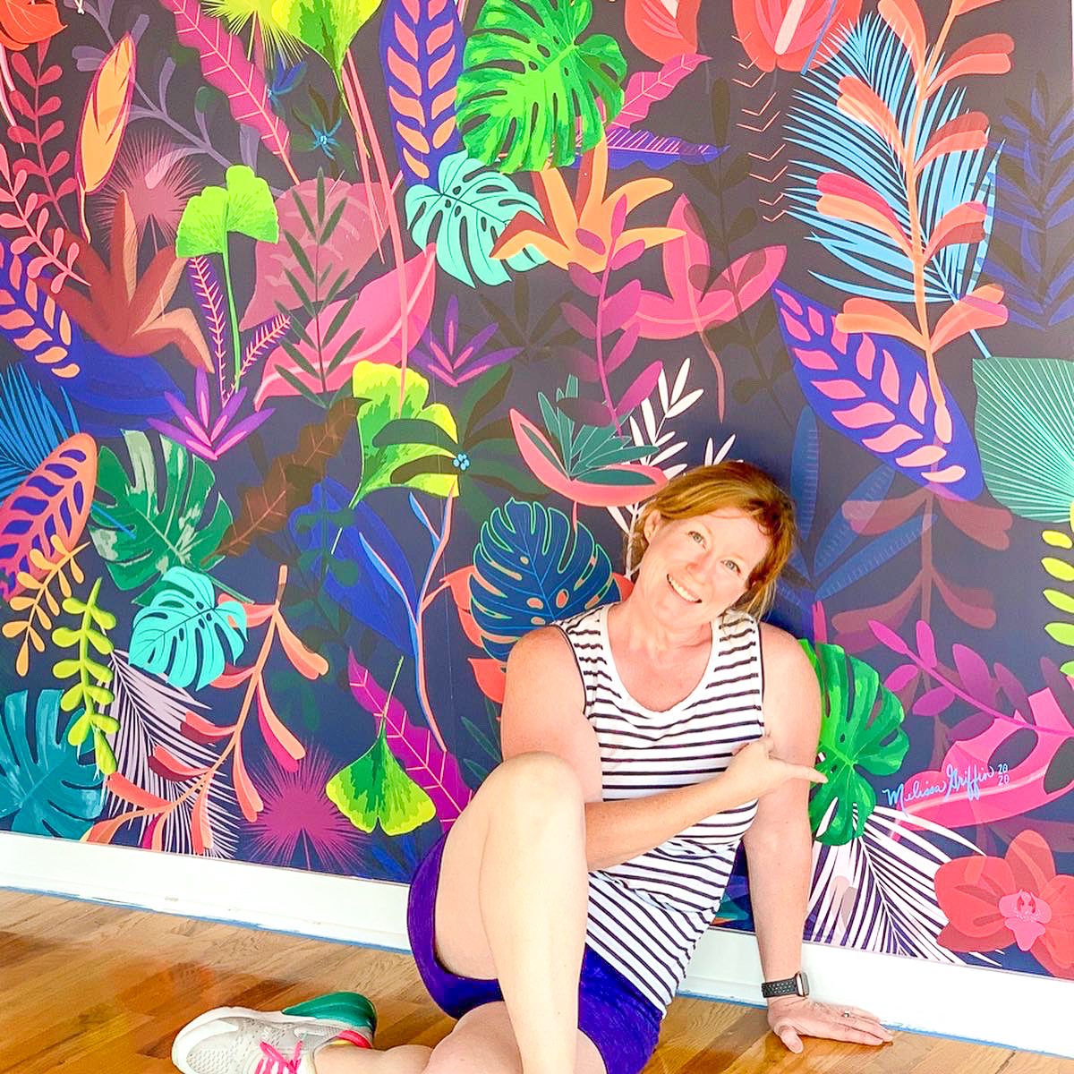 woman in striped shirt and blue shorts sitting by colorful living room wall mural